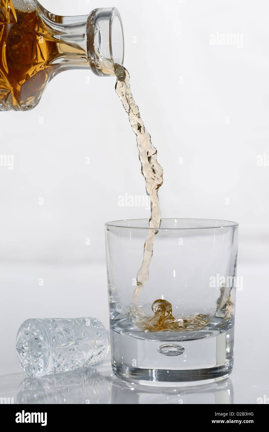 Gießen Whisky von einem Kristall Karaffe in einen tumbler Glas auf weißem Hintergrund Stockfoto