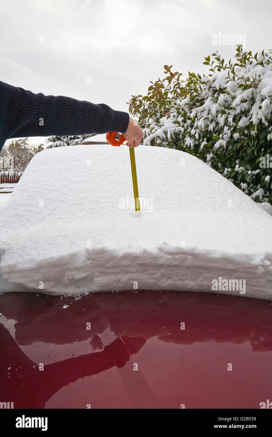 Ein Mann messen, verwenden ein Maßband, um Schneehöhe an seinem Auto zu messen. 220mm oder 8 und einen halben Zoll von Schnee. Stockfoto