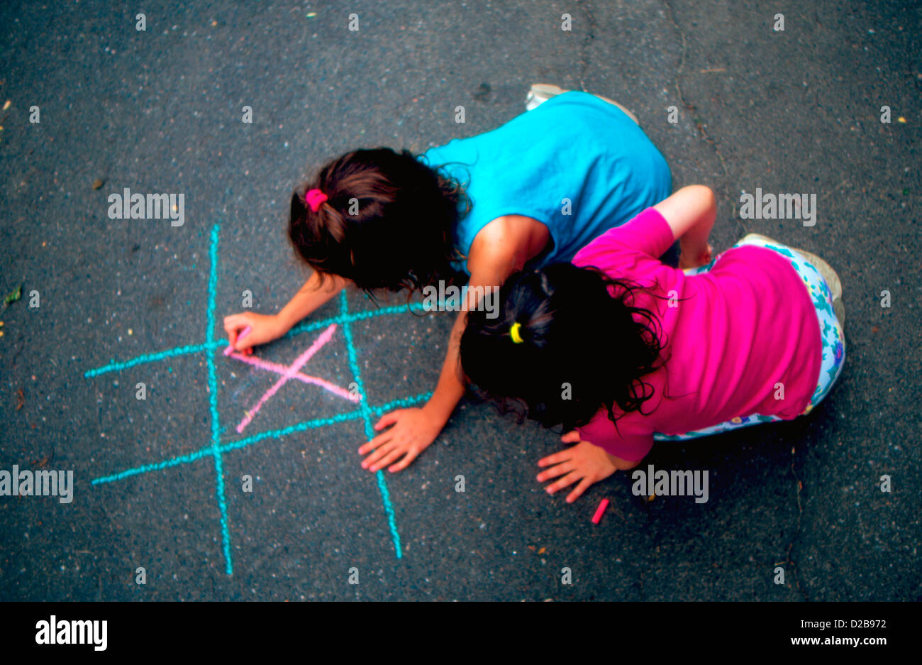 Zwei kleine Mädchen spielen Tic Tac Toe mit farbiger Kreide Stockfoto