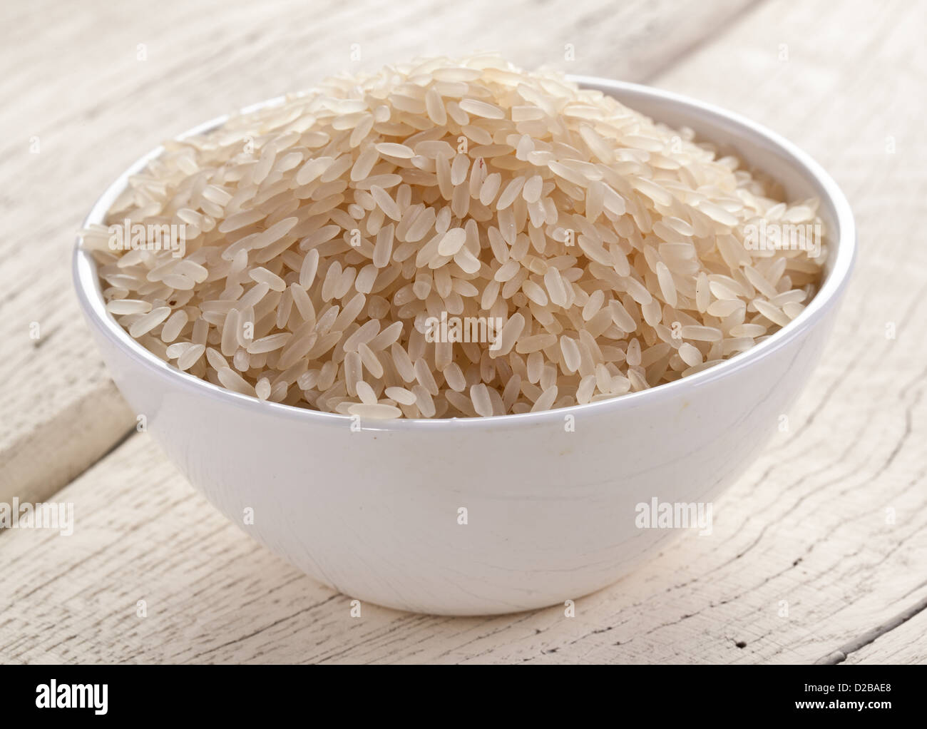 Ungekochten Reis in einer Schüssel auf einem weißen Holztisch. Stockfoto