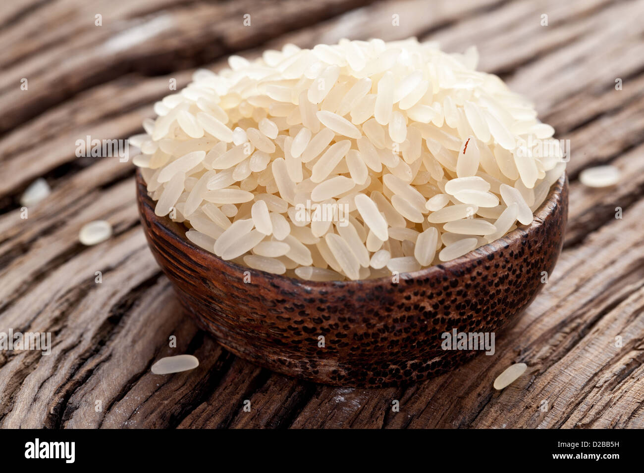 Ungekochten Reis in einer Schüssel auf einem dunklen Holztisch. Stockfoto