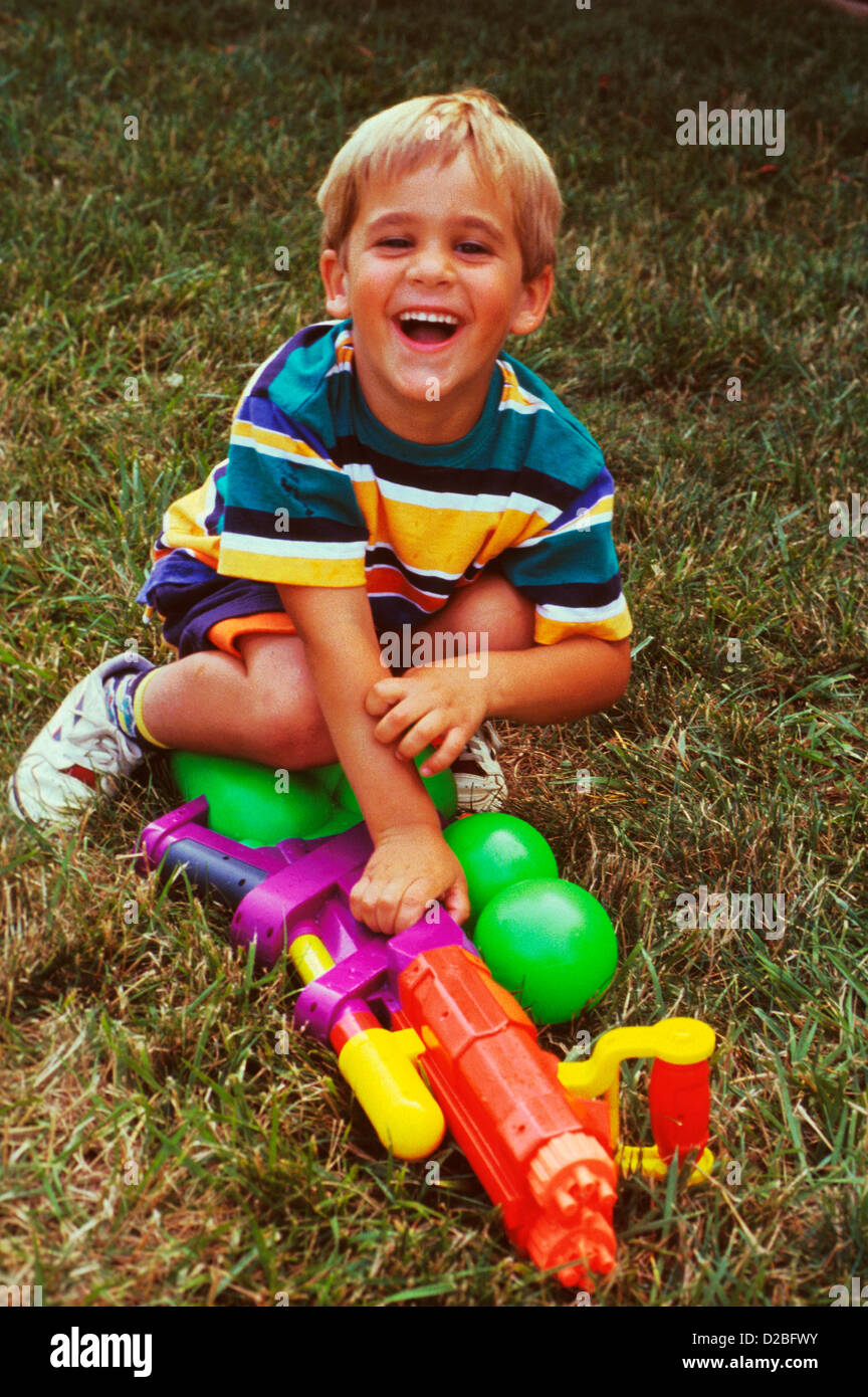 Fünf Jahre alte Blonde junge mit einer Wasserpistole lächelnd In einem Hinterhof Stockfoto