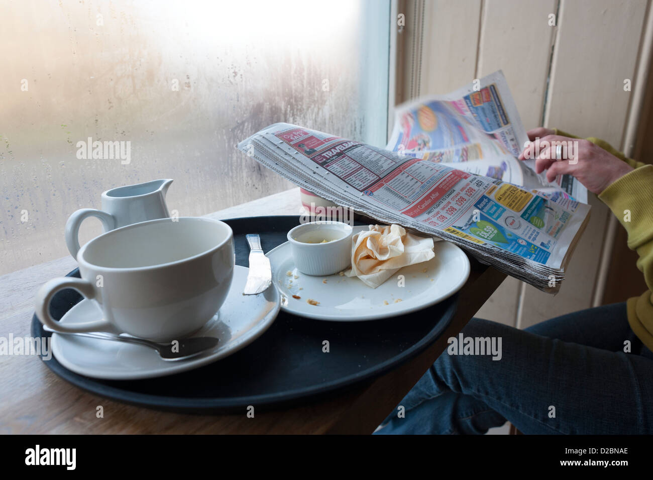 Frau liest Zeitung am Café Fenster mit leeren Becher und Teller, England, UK Stockfoto