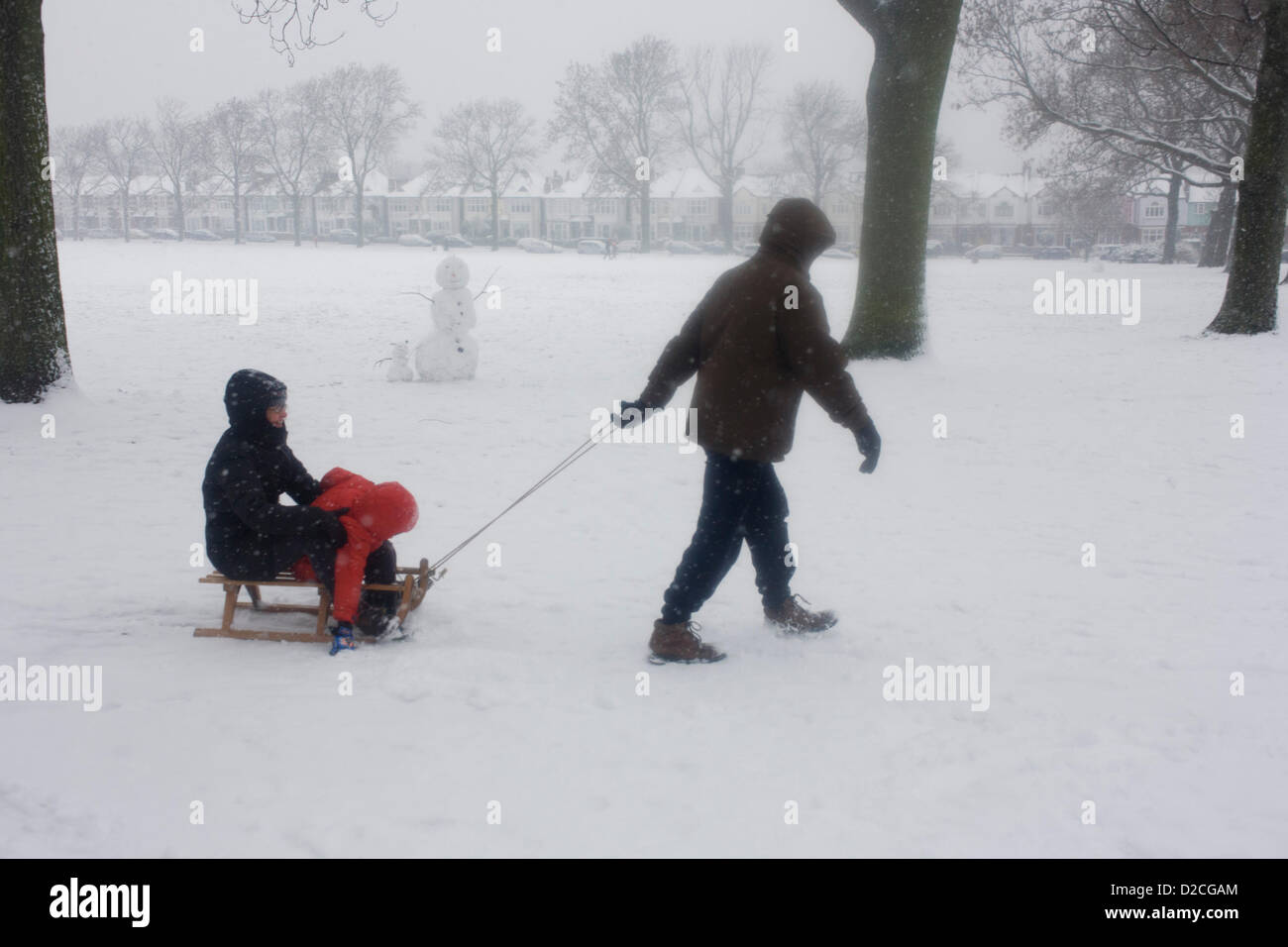 Eine Familie im Schnee genießen ein Wintertag mit ihrem Kind und Schlitten in einer verschneiten South Park in London. Während einer längeren Kälteperiode des schlechten Wetters fiel Schnee kontinuierlich auf das Kapital am Sonntag, so dass Familien die Möglichkeit, die trostlosen Bedingungen genießen hier in Ruskin Park im Stadtteil Lambeth. Ziehen die Mutter und Kind, die auf dem Schlitten fahren, geht der Mann durch Pulver an einem eiskalten Tag wo fällt noch Schnee. Ein Schneemann primitiv gebaut steht im Hintergrund, während weiter unten die Hügel sind Edwardian Periode Häuser unter 100 Jahre alten Eschen. Stockfoto