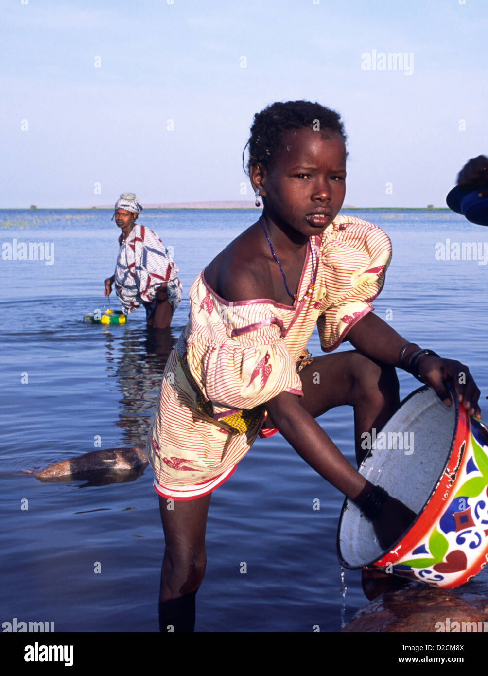 Ein junges Mädchen aus der Volksgruppe Peul von Mali, Westafrika, hilft ihrer Mutter, die die Gerichte in den Fluss Niger zu reinigen. Stockfoto