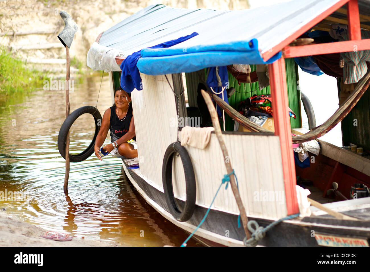 Eine Frau an Bord eines traditionellen Flussschiffes auf dem Amazonas, in der Nähe eines abgelegenen Dorfes, wäscht am Ufer des Wassers und zeigt das tägliche Leben im Regenwald Stockfoto