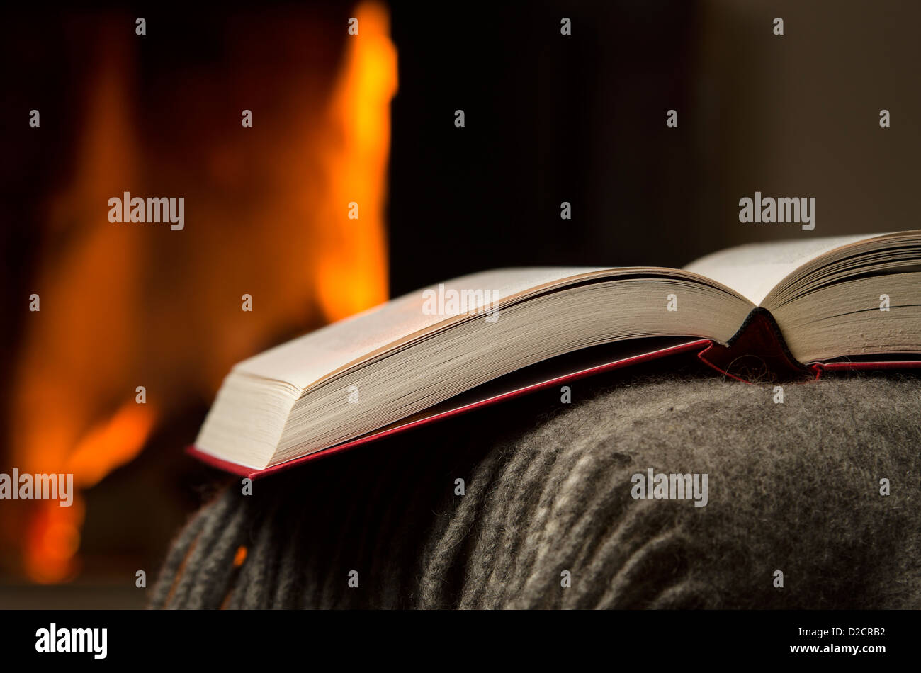 Friedliche Closeup aufgeschlagenen Buches auf eine Armlehne der Couch ausruhen. Warmen Kamin auf Hintergrund. Stockfoto