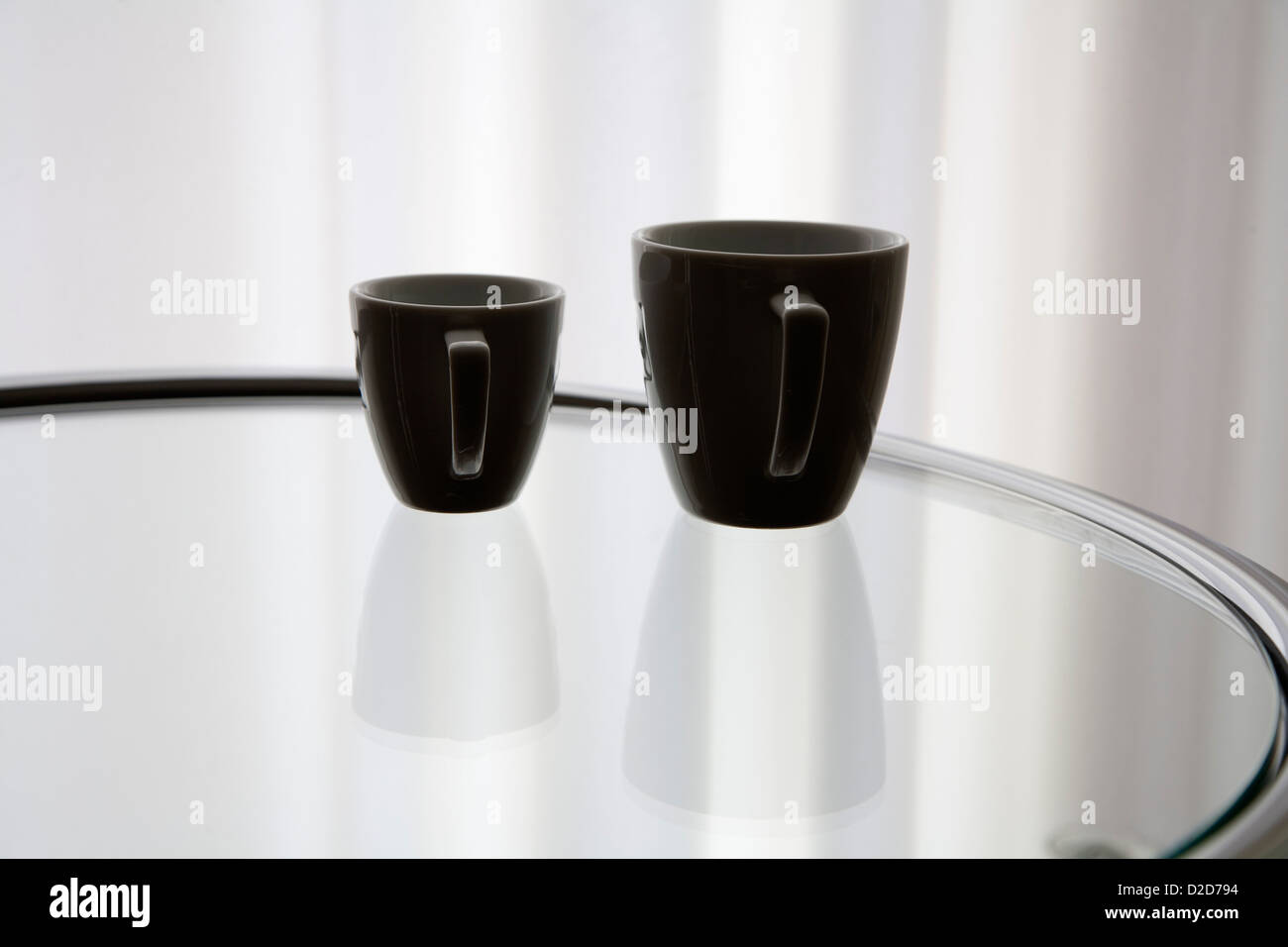 Eine Kaffeetasse und eine Espressotasse reflektiert auf einem Glastisch Stockfoto