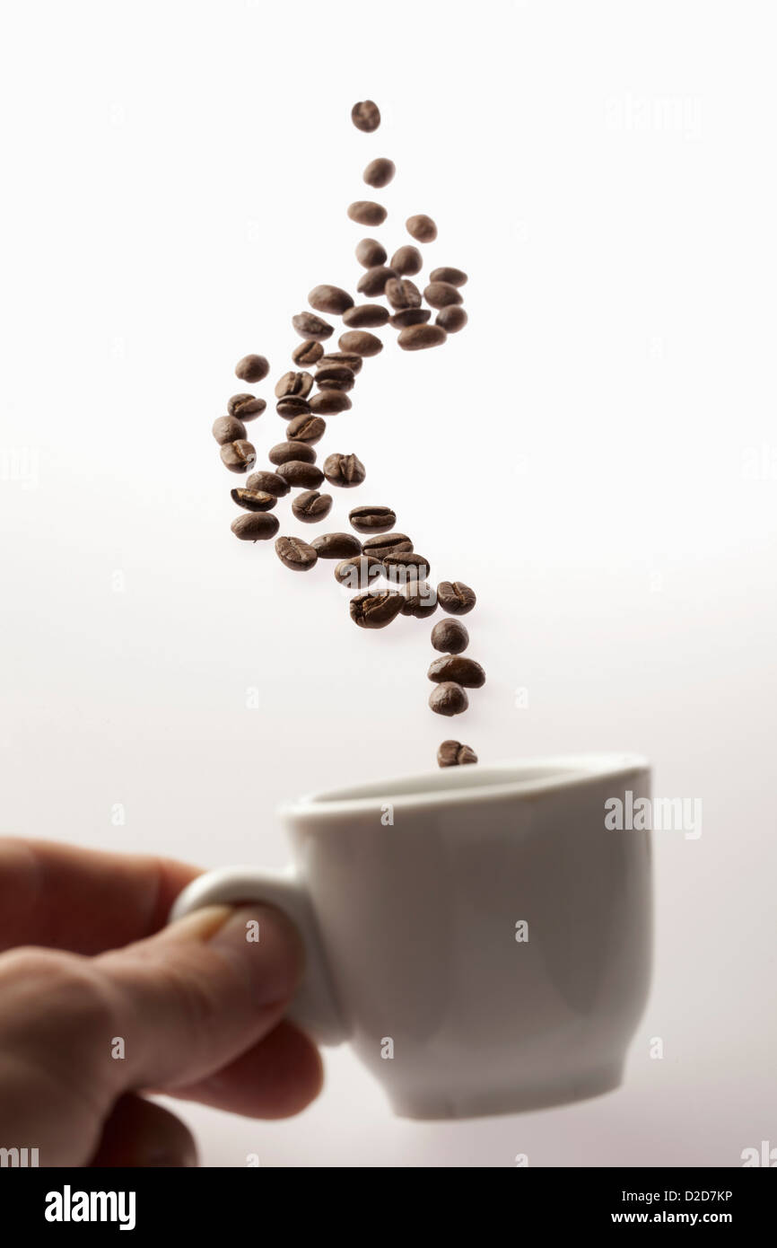 Ein Mann hält eine Kaffeetasse mit schwebenden Kaffeebohnen Stockfoto