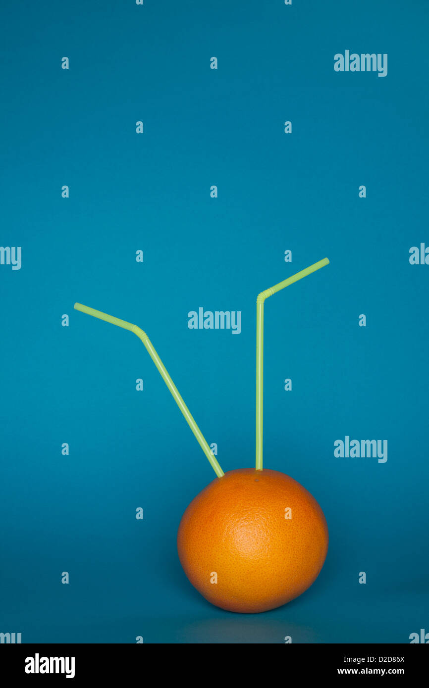 Eine Orange mit zwei Trinkhalmen hinein stecken Stockfoto