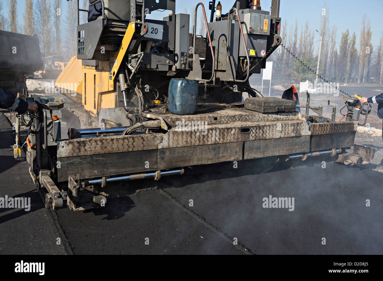 Manuelle Arbeiter, die Kontrolle der großen Straßenbelag-Maschine wird gefolgt von Sattelschleppers Stockfoto
