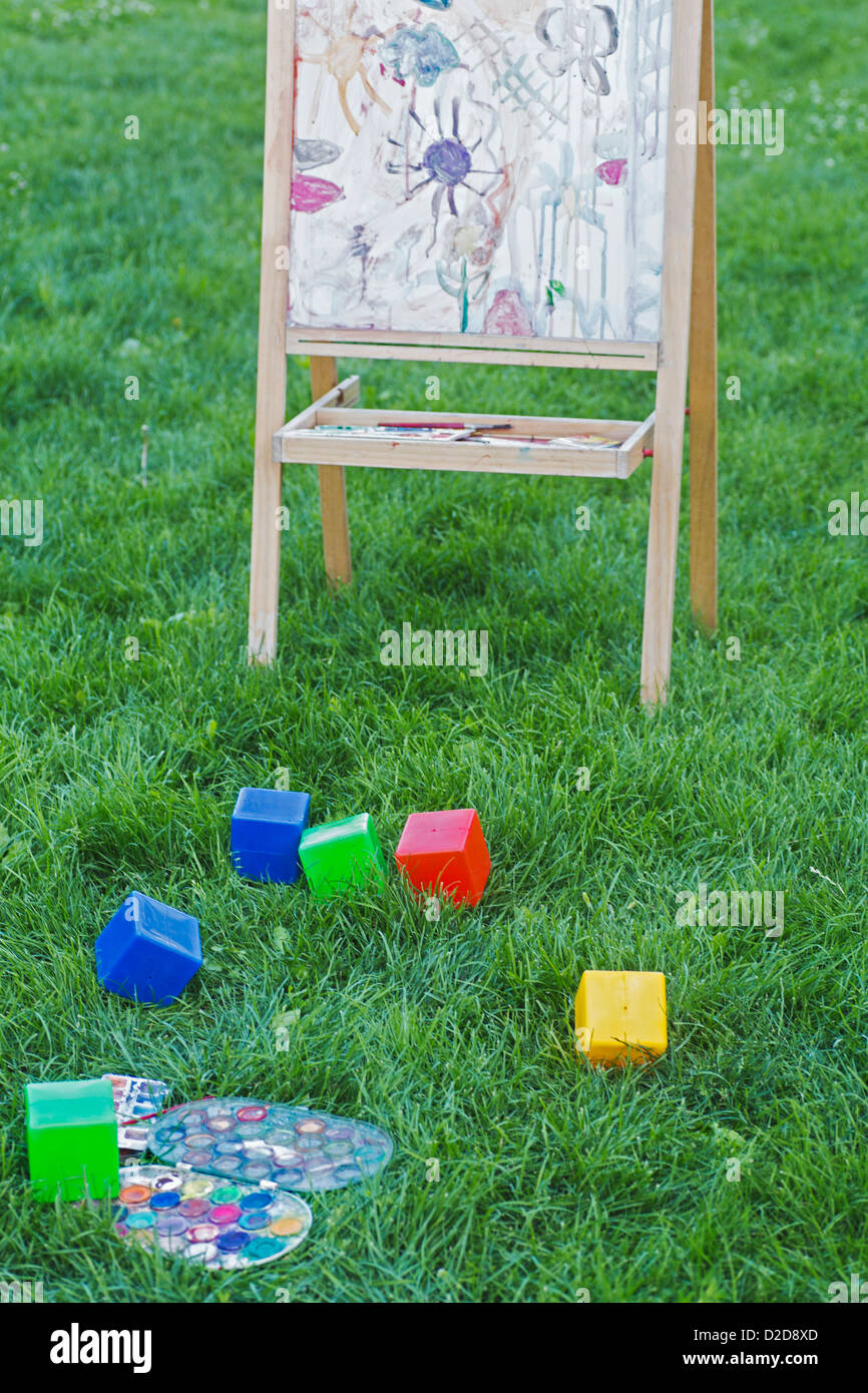 Eine Staffelei, Bauklötze und Aquarellfarben auf der Wiese von einem Hinterhof Stockfoto