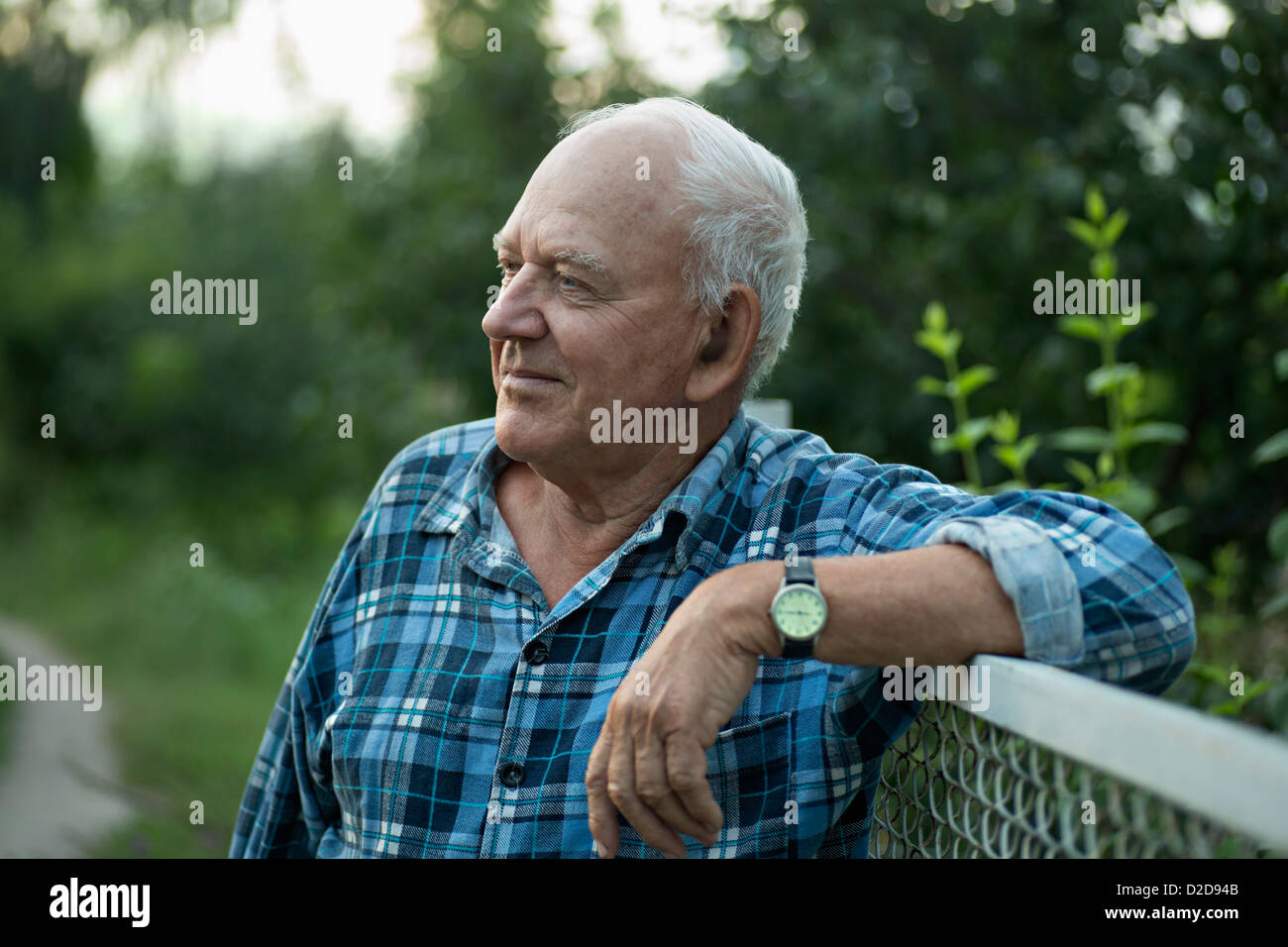 Ein senior Mann an einen Zaun gelehnt und heiter wegschauen Stockfoto