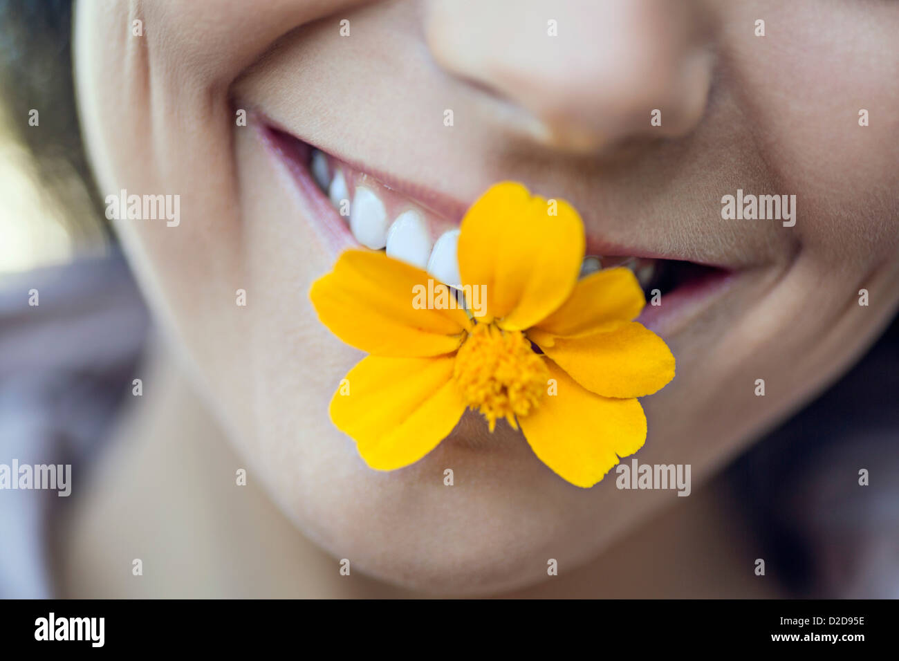 Eine junge grinsenden Frau, die eine einzelne Blume im Mund Stockfoto