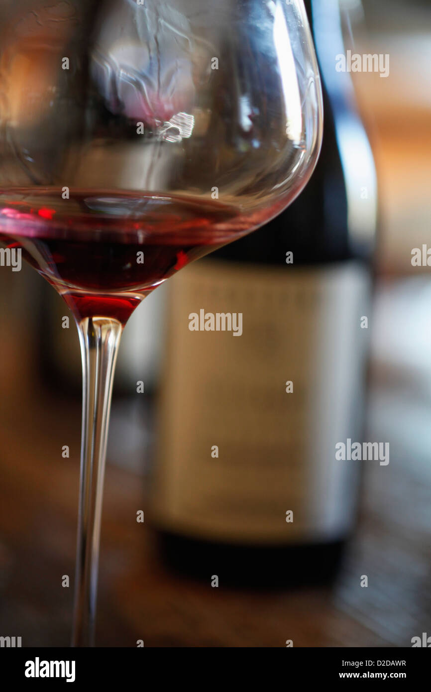 Ein Weinglas mit Rotwein und zwei Flaschen Wein im Hintergrund Stockfoto