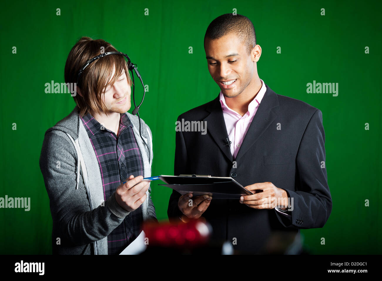 Floor-Manager führt durch Skripte mit einer TV-Moderatorin in einem Greenscreen-Studio. Stockfoto