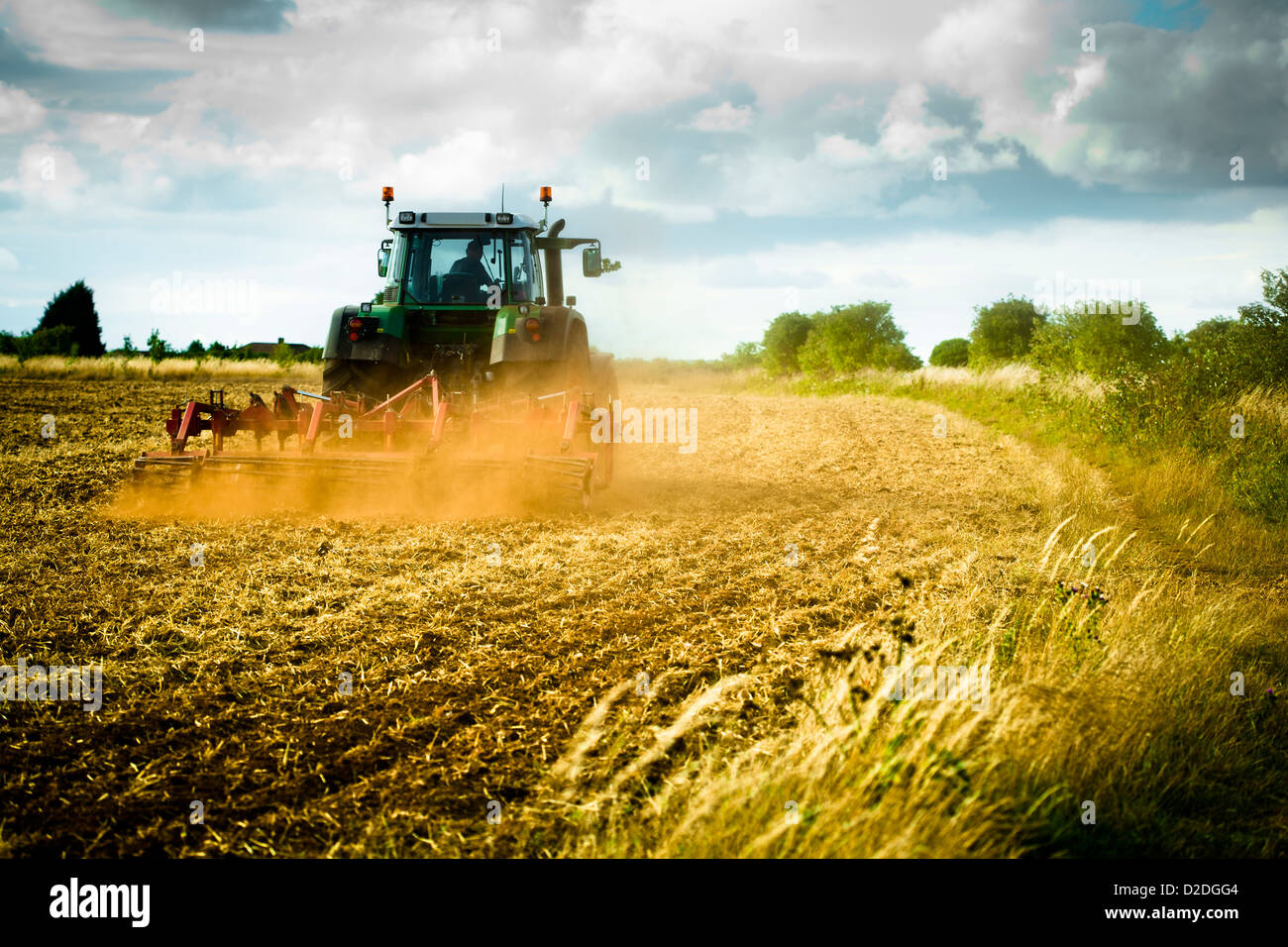 Traktor pflügen ein Feld mit einer Spur von Staub hinter sich. Stockfoto