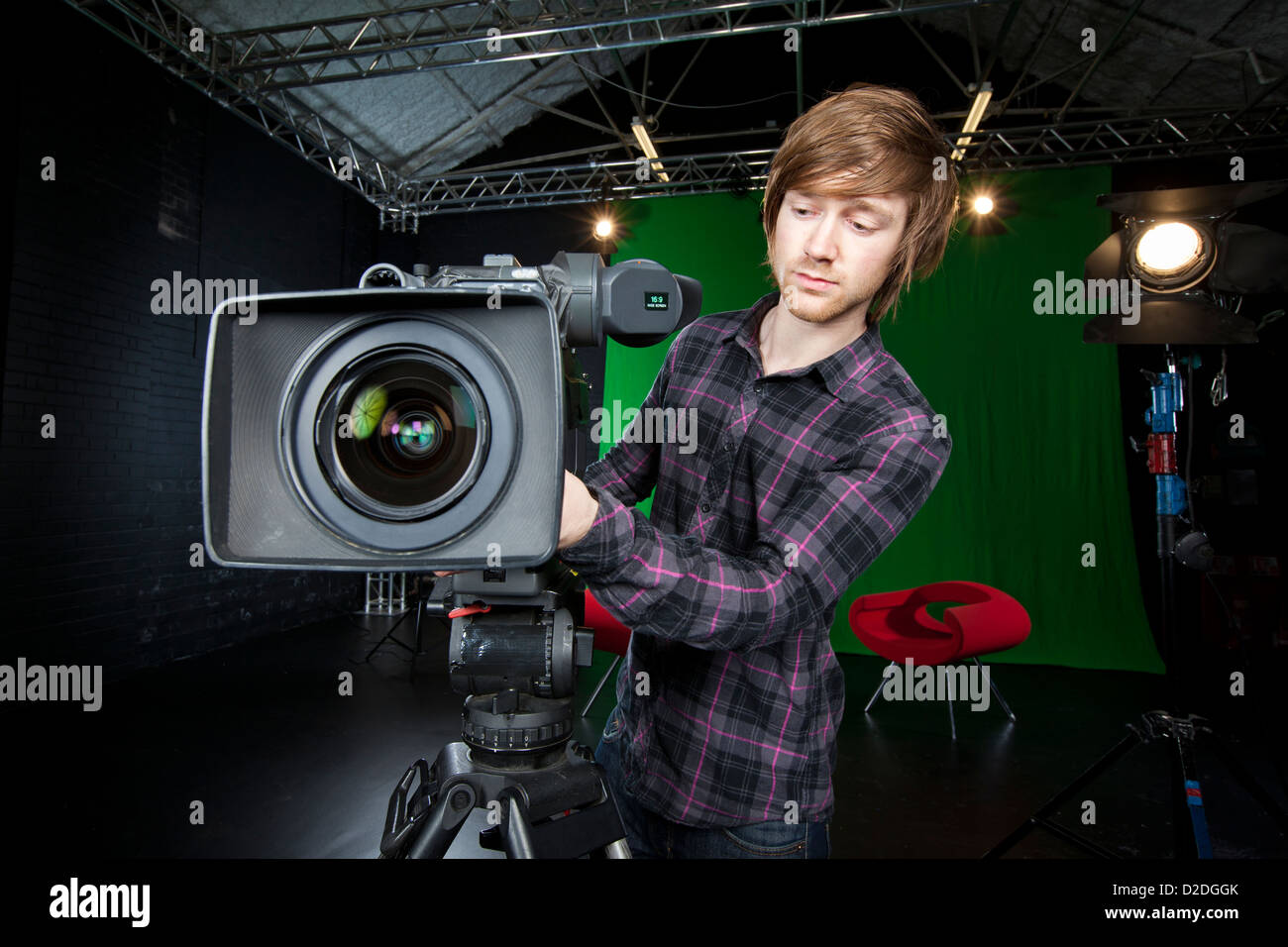 Junger Mann bereitet eine TV-Studio-Kamera mit Studioleuchten und CSO grünen Vorhang im Hintergrund Stockfoto