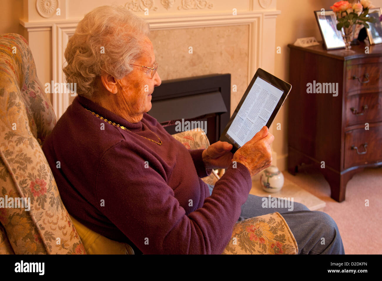 Ältere Frau Rentner mit Brille auf Apple Ipad Tablet zu Hause relaxen am Stuhl und Las Zeitung online Stockfoto