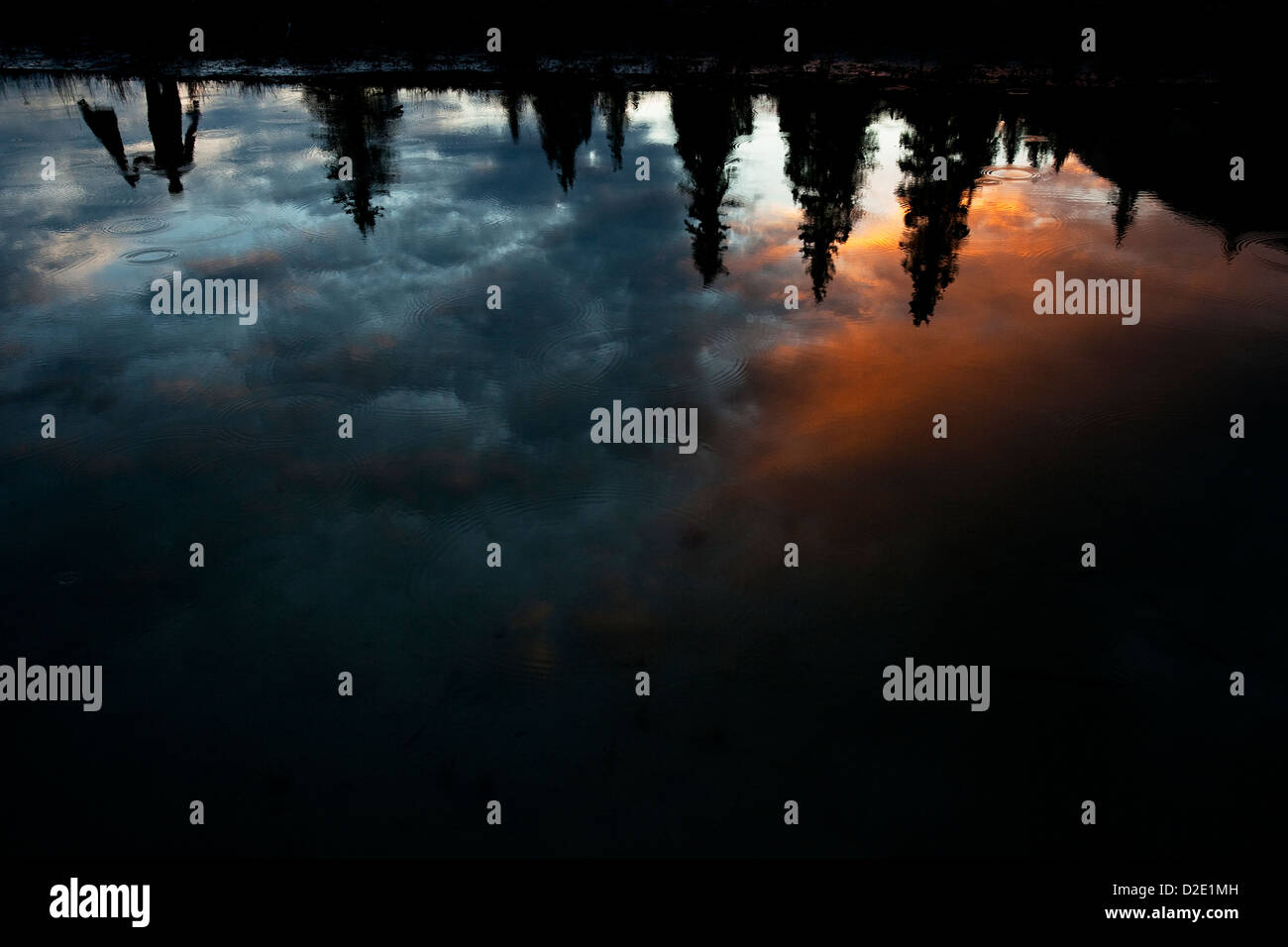 Ein Mann kopfüber in einen See mit bunten Wolken und Regentropfen reflektiert. Stockfoto