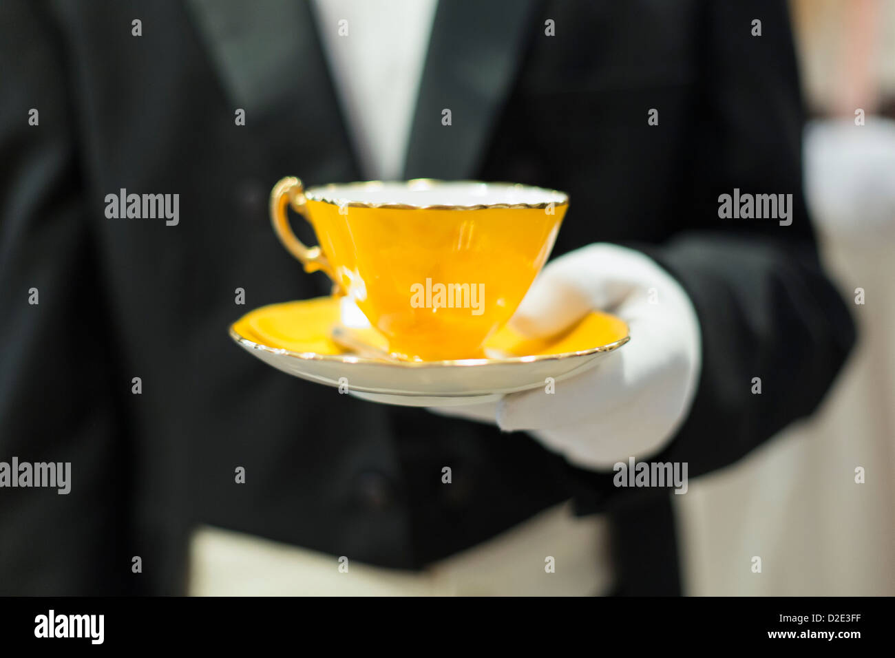 weiße behandschuhte Hand hält ein gelber Teetasse und Untertasse Stockfoto