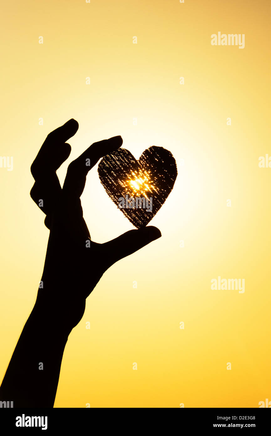 Mädchen Hand hält Herzform bei Sonnenuntergang. Silhouette Stockfoto