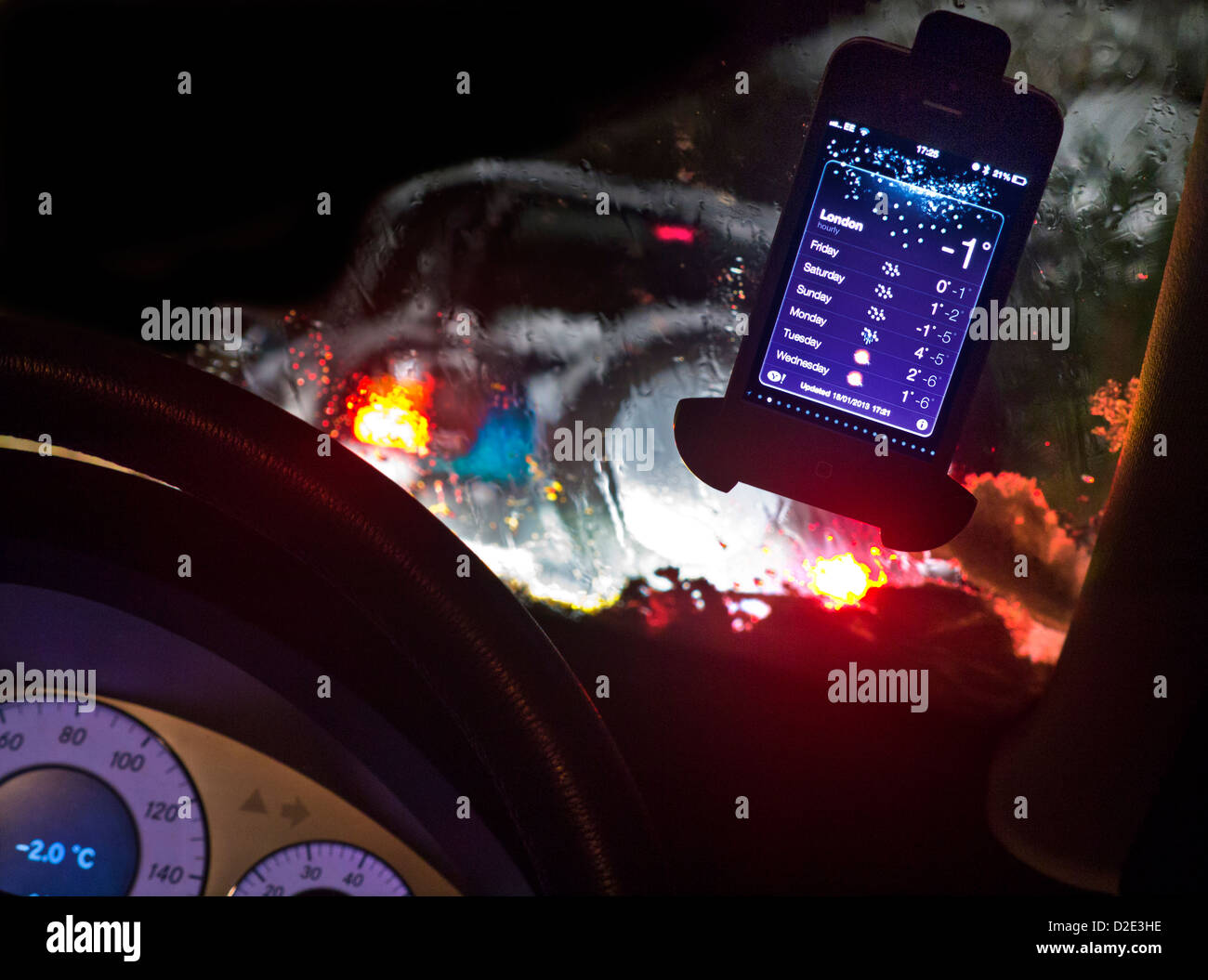Das iPhone auf der Windschutzscheibe des Autos zeigt bei Nacht eine Schneewarnung und eine Temperatur von minus 2 °C im Verkehr mit gefährlichen Fahrbedingungen an Stockfoto