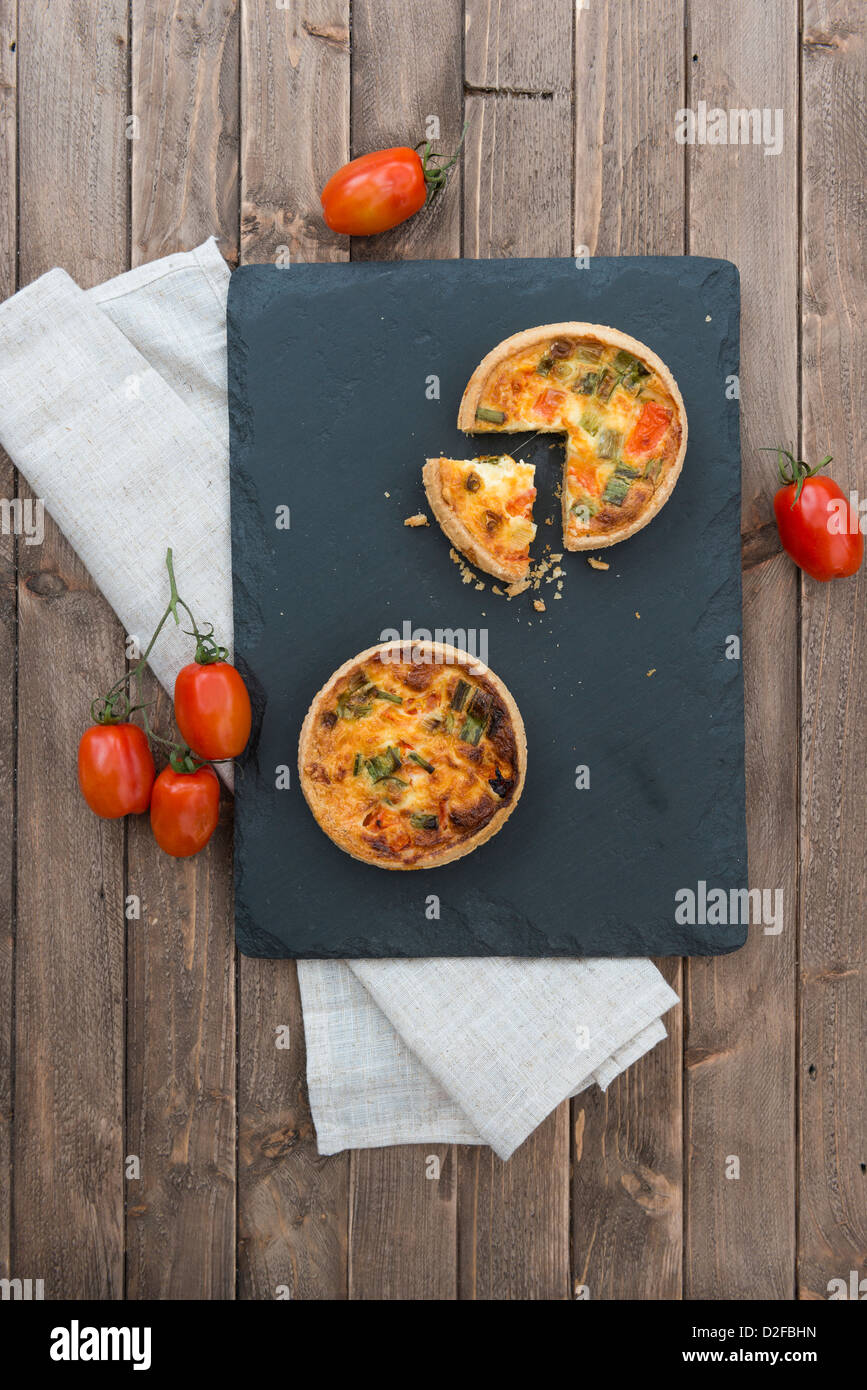 Gekochter Käse, Frühlingszwiebeln und Tomaten-Quiche, auf einer Schiefertafel Tafel, garniert mit Tomaten. Stockfoto