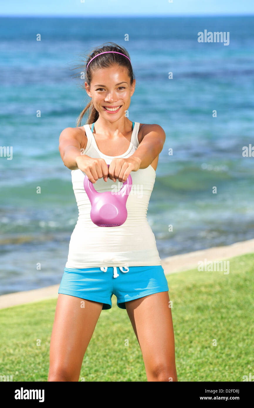 Porträt von schönen jungen Fit Frau heben Kettlebell während Stärke Training Bewegung in der Natur auf dem Rasen am Meer Stockfoto