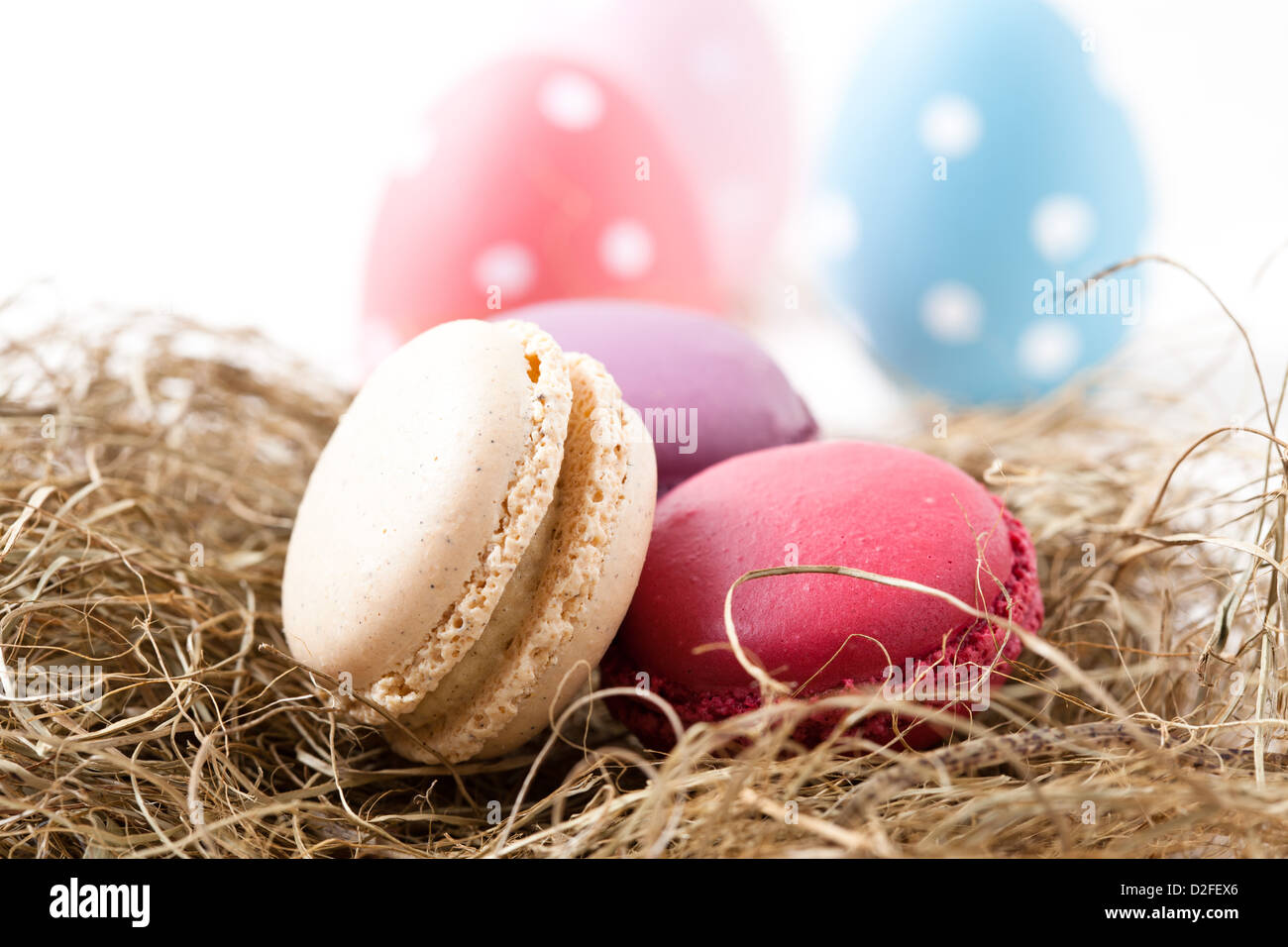 Nahaufnahme von bunten Macarons ruht im Stroh Nest und Easter Eggs auf hellem Hintergrund Stockfoto