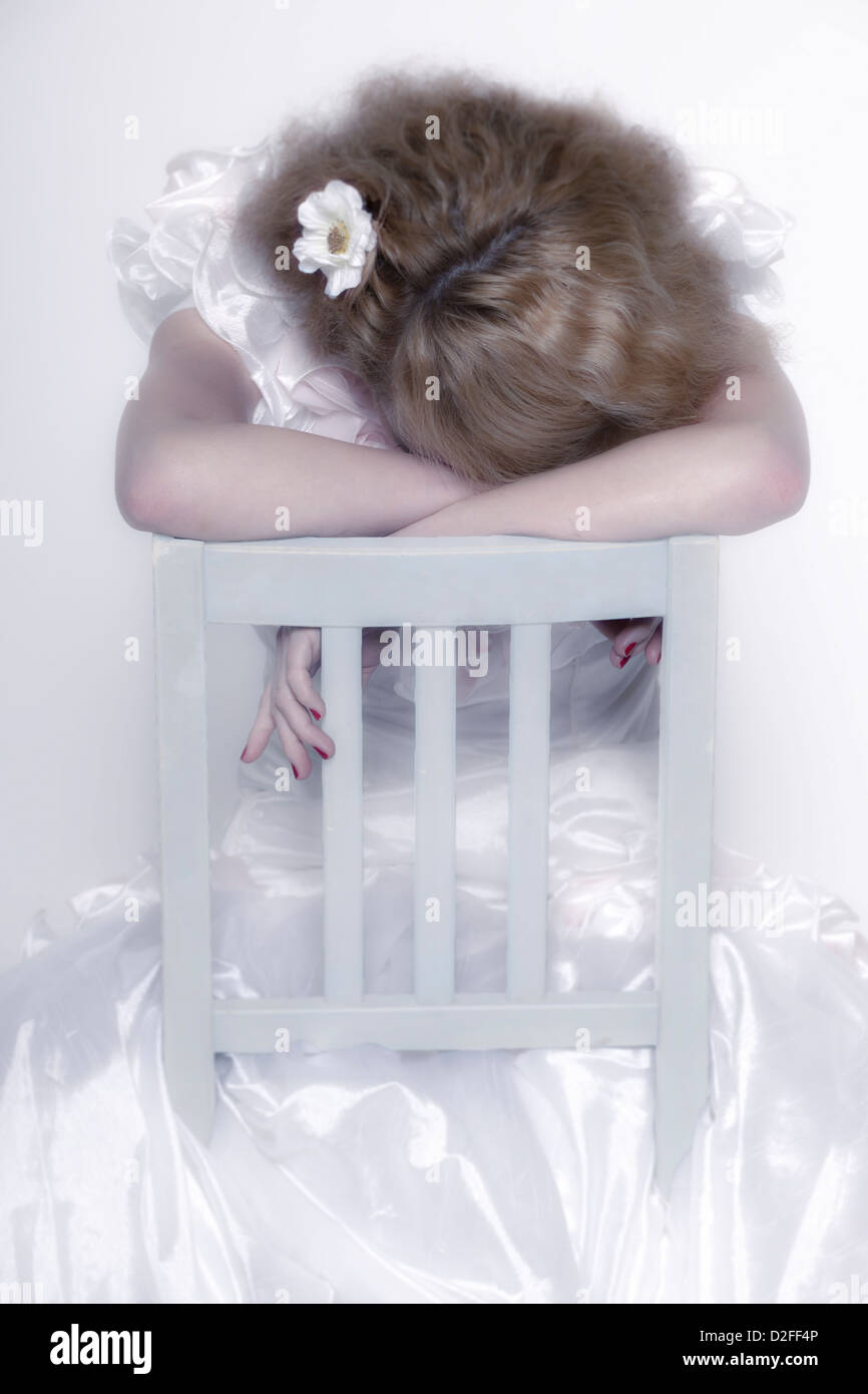 eine Frau in einem weißen Kleid auf einen weißen Stuhl sitzt und weint Stockfoto