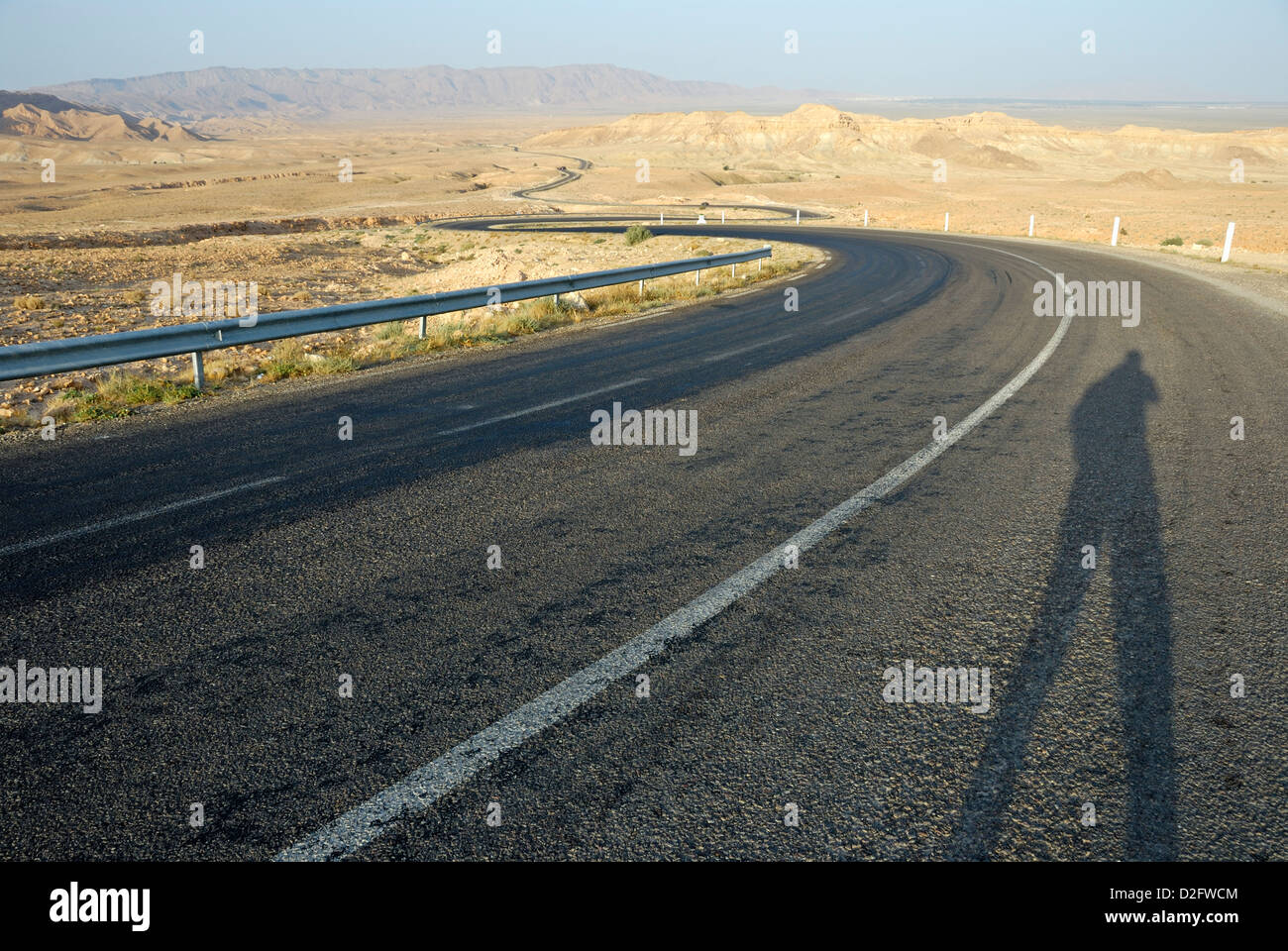 Man Schatten auf einen leeren Wicklung Wüste Straße, Tunesien Stockfoto