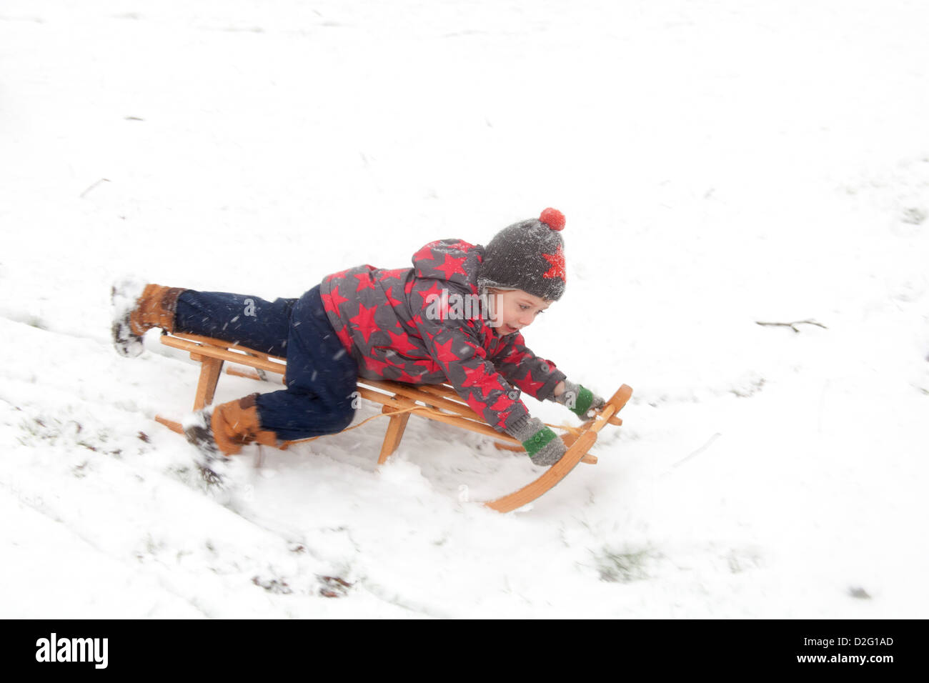 Drei Jahre alter Junge draußen spielen im Schnee auf einem Schlitten. Alresford Hampshire, England, Vereinigtes Königreich. Stockfoto