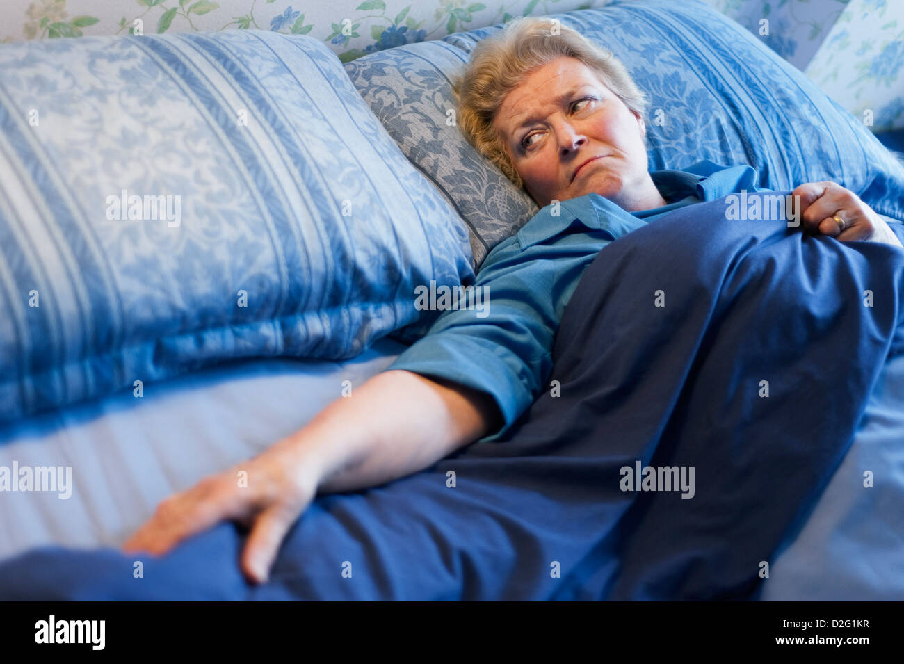 Reife Frau im Bett allein liegen und Blick auf den leeren Platz neben ihr Stockfoto