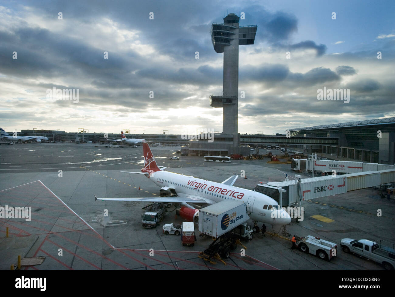 Eine Jungfrau Amerika Airbus A320 Jet steht Flugzeuge vor dem Kontrollturm in der Dämmerung, wie es geladen mit Essen ist und von LSG Sky Chefs am John F. Kennedy Airport, JFK Airport, New York, USA beliefert Stockfoto