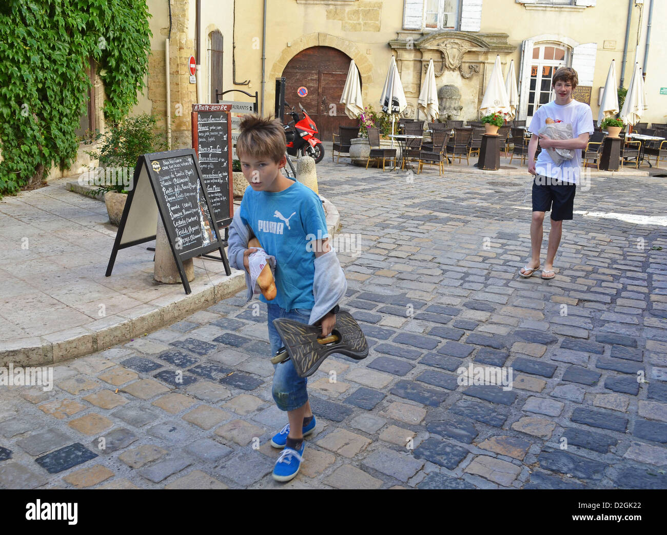 2 Jungs mit Skateboards Rückkehr aus einem Sonntagmorgen Reise in die Bäckerei in Lourmarin Frankreich Stockfoto