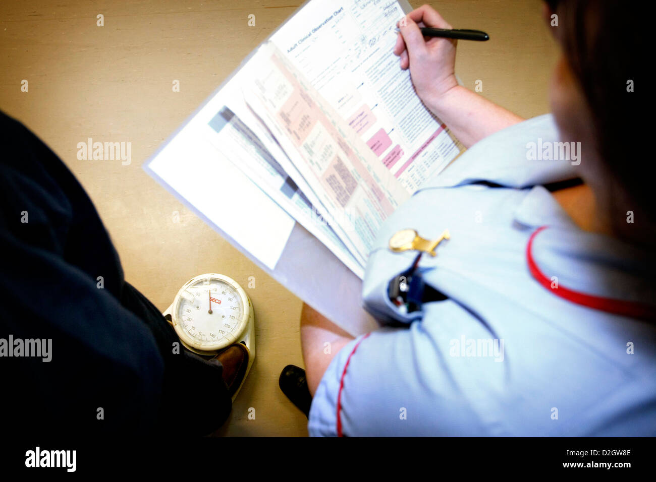 Patienten stehen auf Skalen, während Pflegepersonal Gewicht und Dokument in Patienten Noten studieren Stockfoto