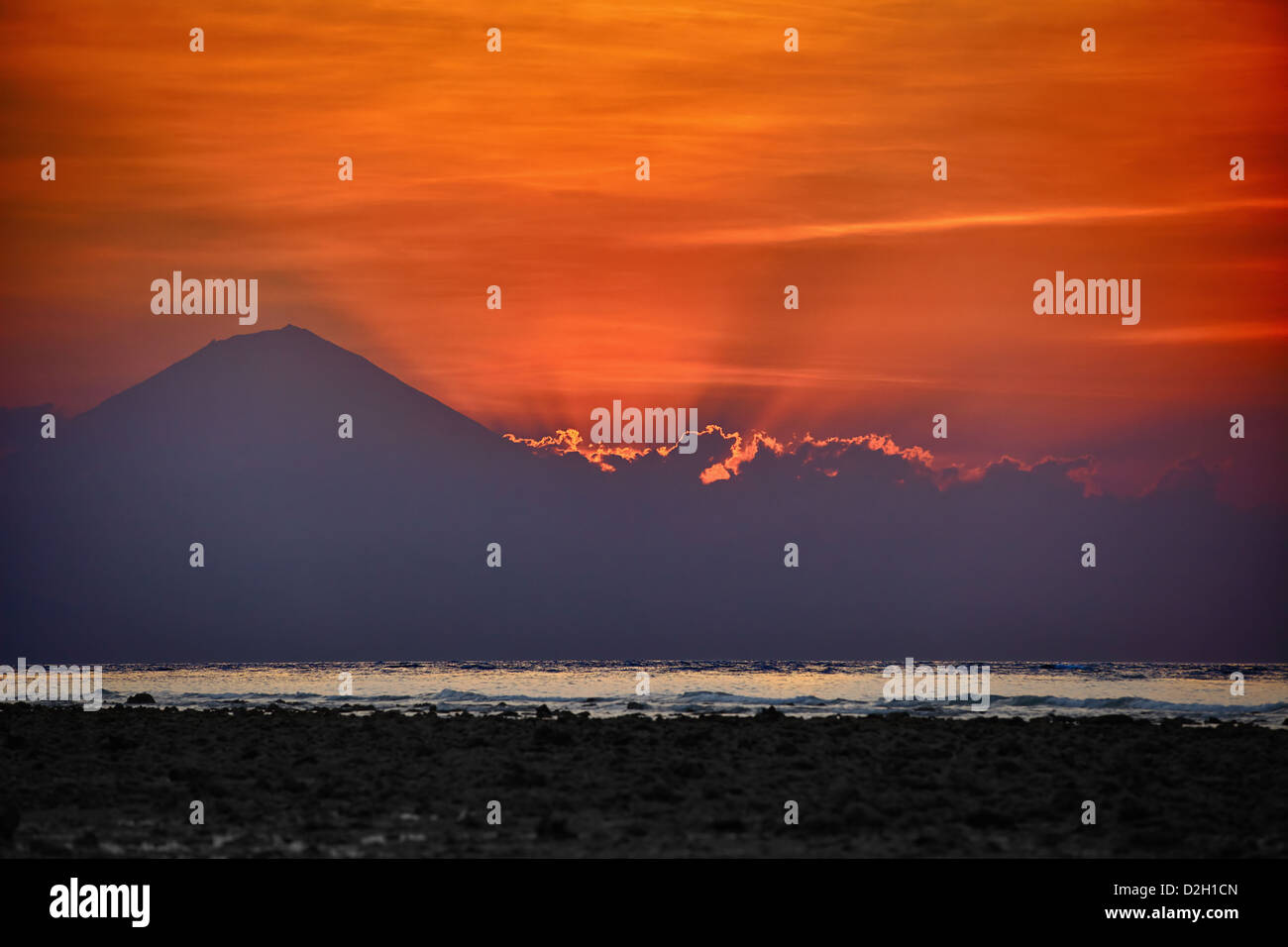 Surrealistische Sonnenuntergang hinter dem Vulkan und Wolken mit roten Himmel auf Hintergrund und Meer auf Vorderseite Stockfoto