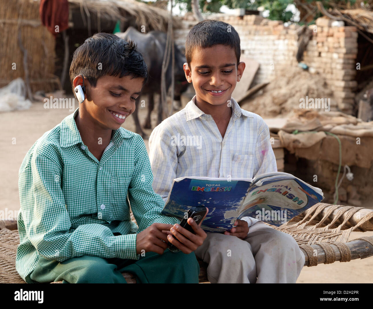 Indien, Agra, Kind in der Schule uniform mit Smartphone, tragen Bluetooth-Kopfhörer und Bruder lesen Englisch Lehrbuch Stockfoto