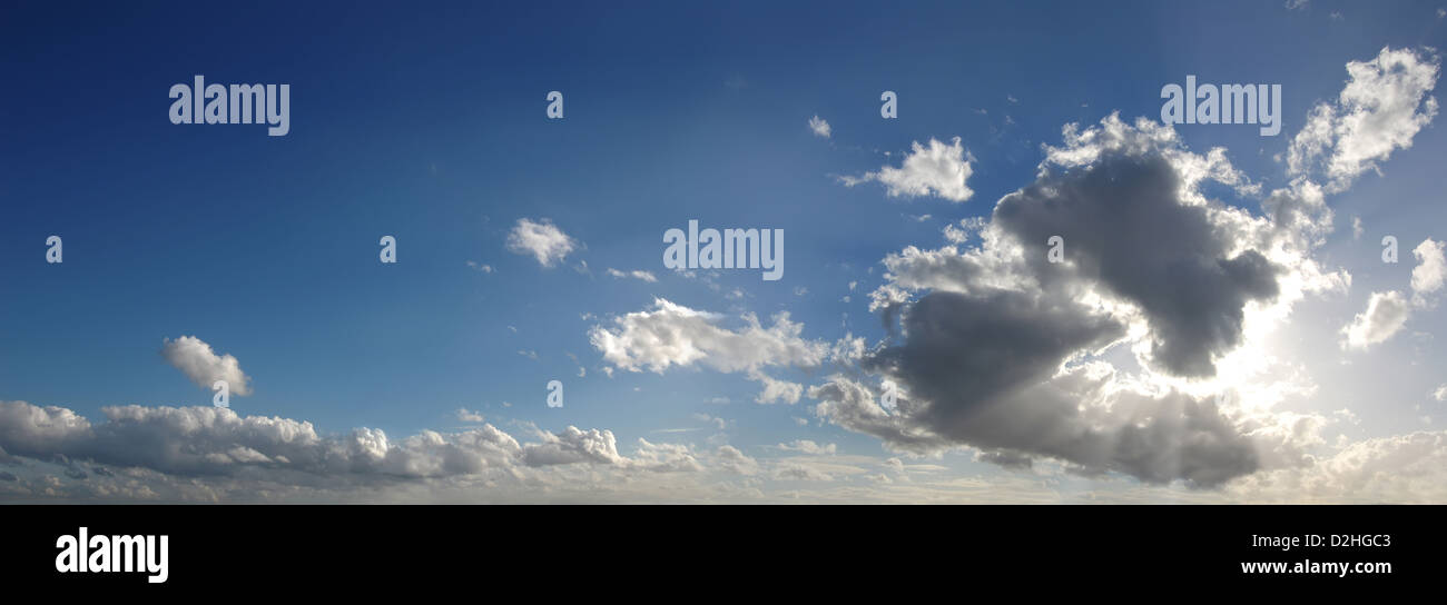 Blauer Himmel mit einigen Cumulus-Wolken im Hintergrund und einer großen Wolke, die Maskierung der Sonne, im Vordergrund einige Gott Strahlen erzeugen Stockfoto