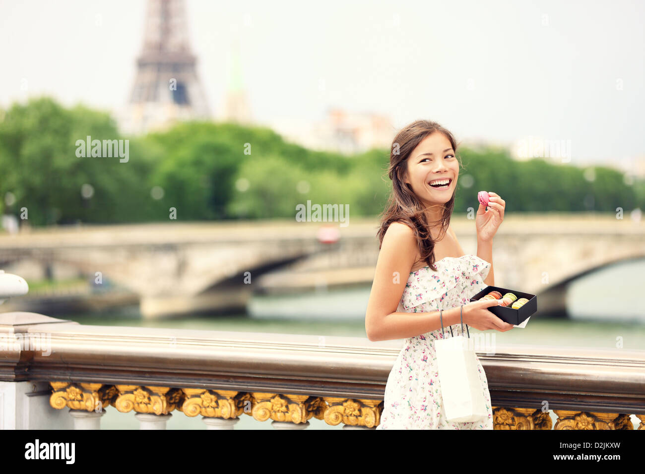 Lächelnde süße Frau Essen Französisch Gebäck Macaron in Paris mit Eiffelturm und Pont des Invalides im Hintergrund Stockfoto