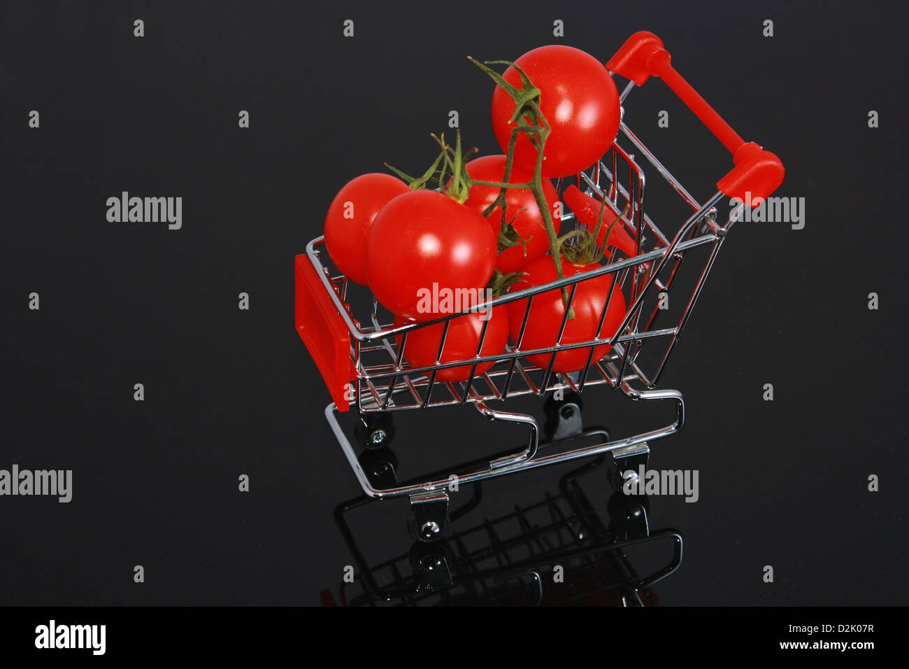 Bio-Tomaten im kleinen Warenkorb auf horizontale Spiegelung auf schwarzem Hintergrund isoliert Stockfoto