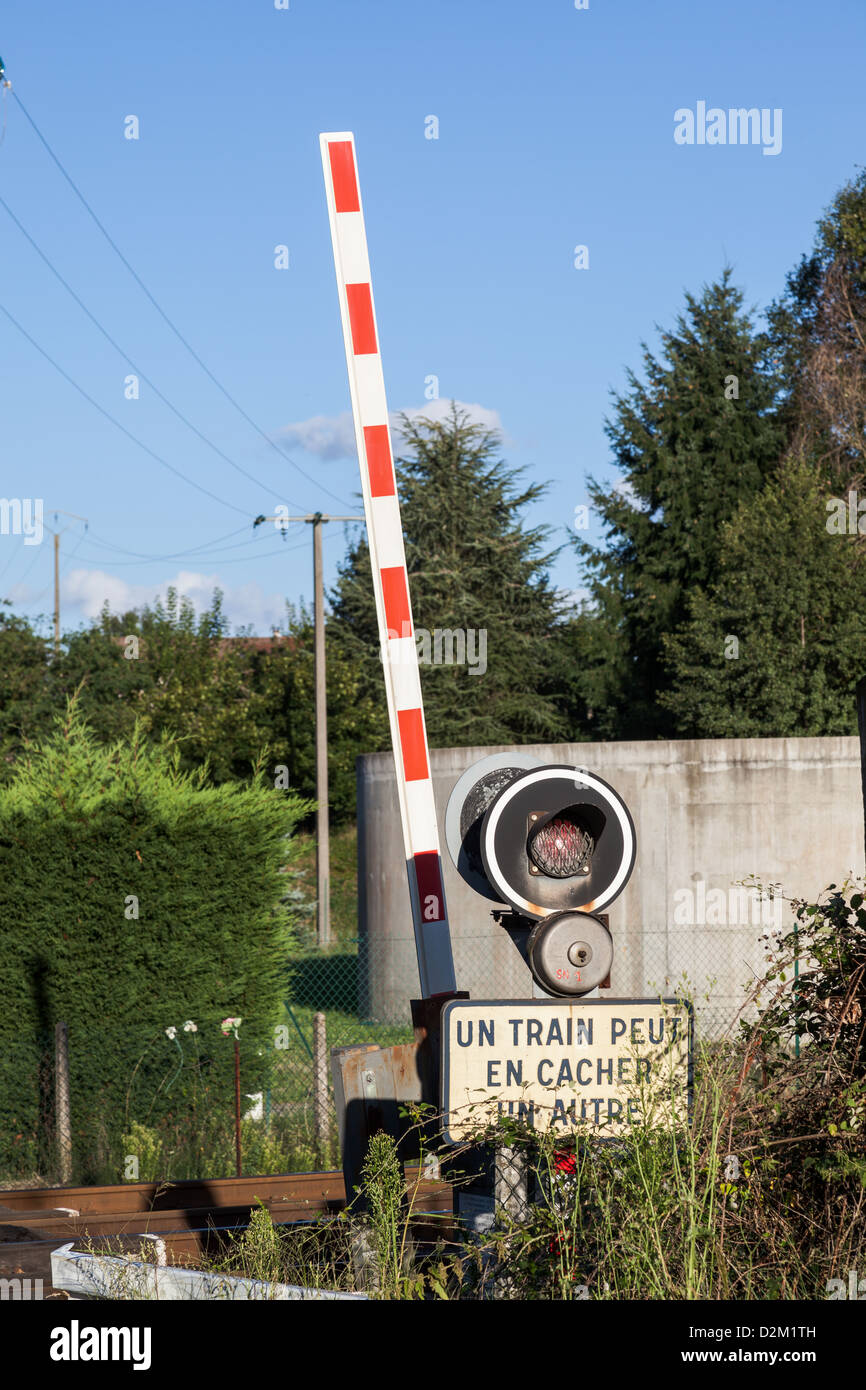 Bahnübergang mit Schild mit der Aufschrift UN train Peut En Cacher un Autre "in Veauche in Rhône-Alpes Region von Frankreich Stockfoto