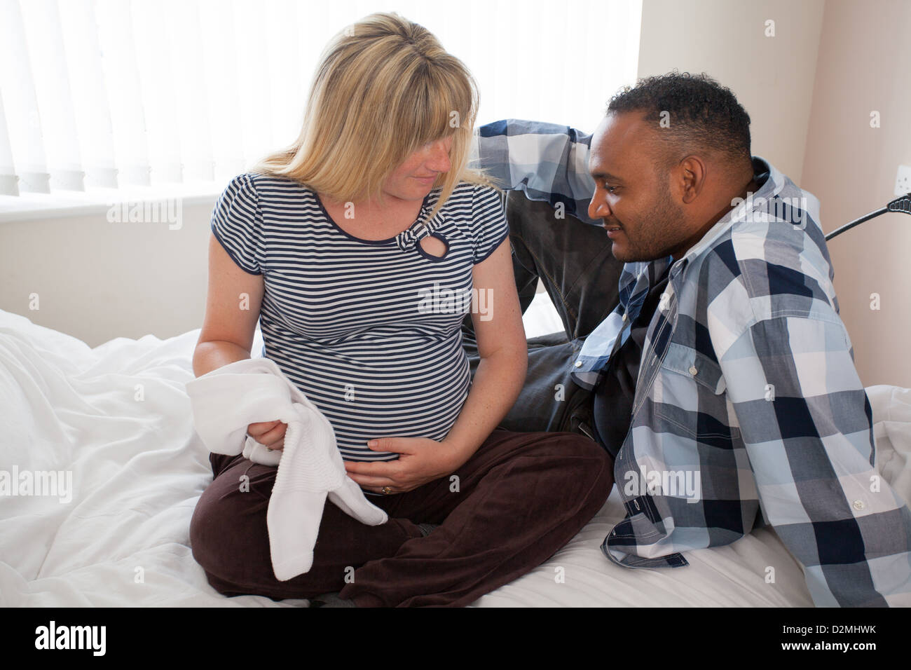 Schwangere weiße weibliche und schwarze männliche halten Baby-Kleidung Stockfoto