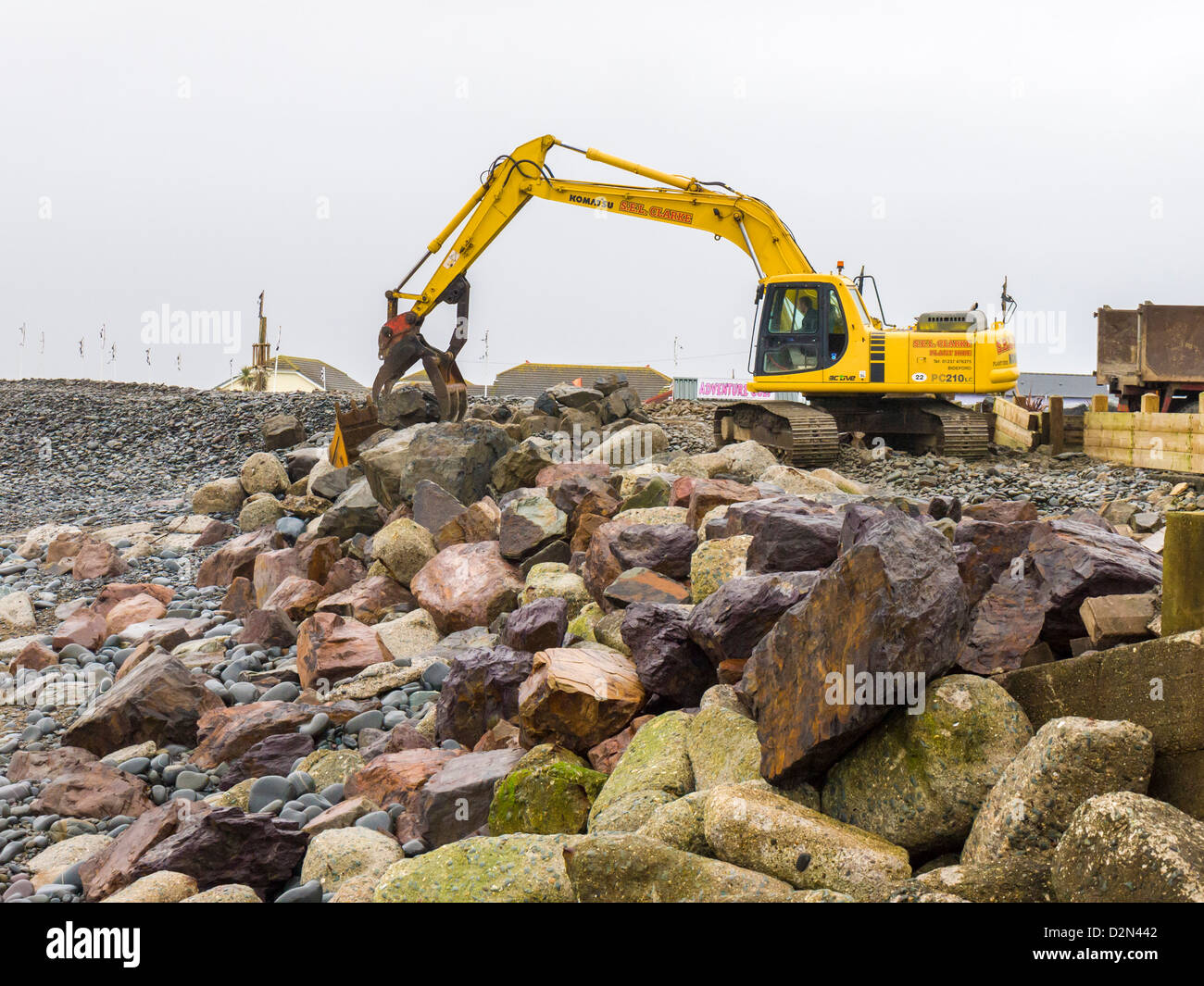 Eine mechanische Digger wird verwendet, um die Wartung und die Reparatur des Meer Abwehr auf dem Kiesel Ridge auf Westward Ho zu verpflichten! Strand. Devon, England. Stockfoto