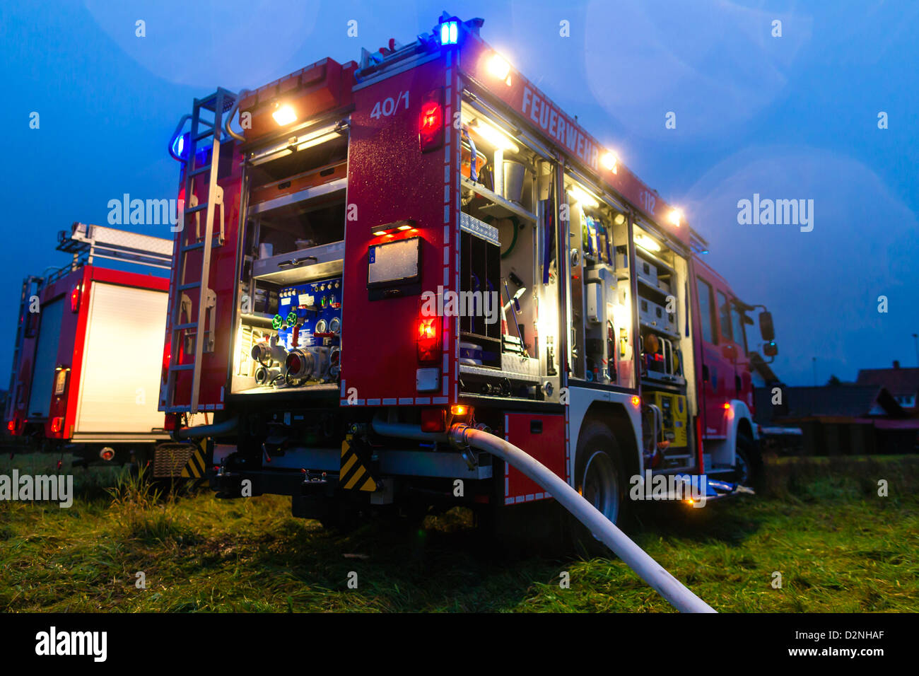Feuerwehr LKW oder Motor mit blinkenden Lichtern, Beleuchtung und Schlauch in Dämmerung, einsatzbereit Stockfoto