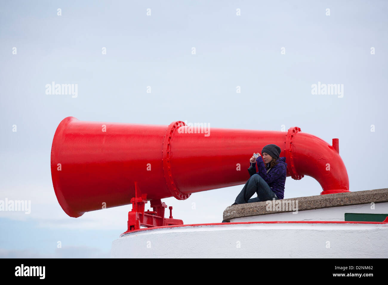 Eine junge Frau sitzt vor dem großen roten Nebelhorn am Cape Wrath Leuchtturm an der nordwestlichen Ecke von Schottland Stockfoto