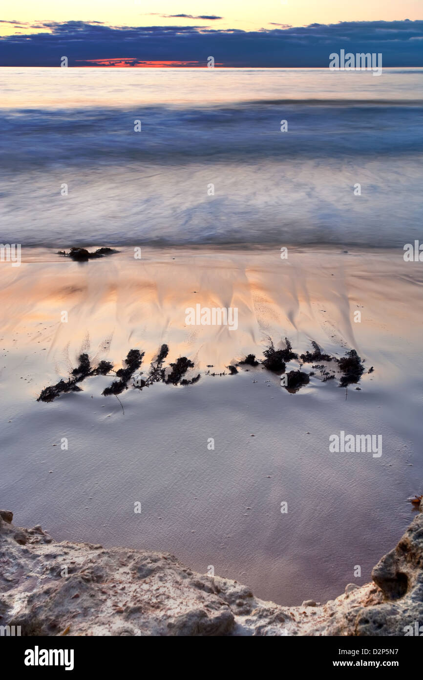 Coastal Sonnenuntergang mit Wellen brechen über dem sandigen Ufer. Stockfoto