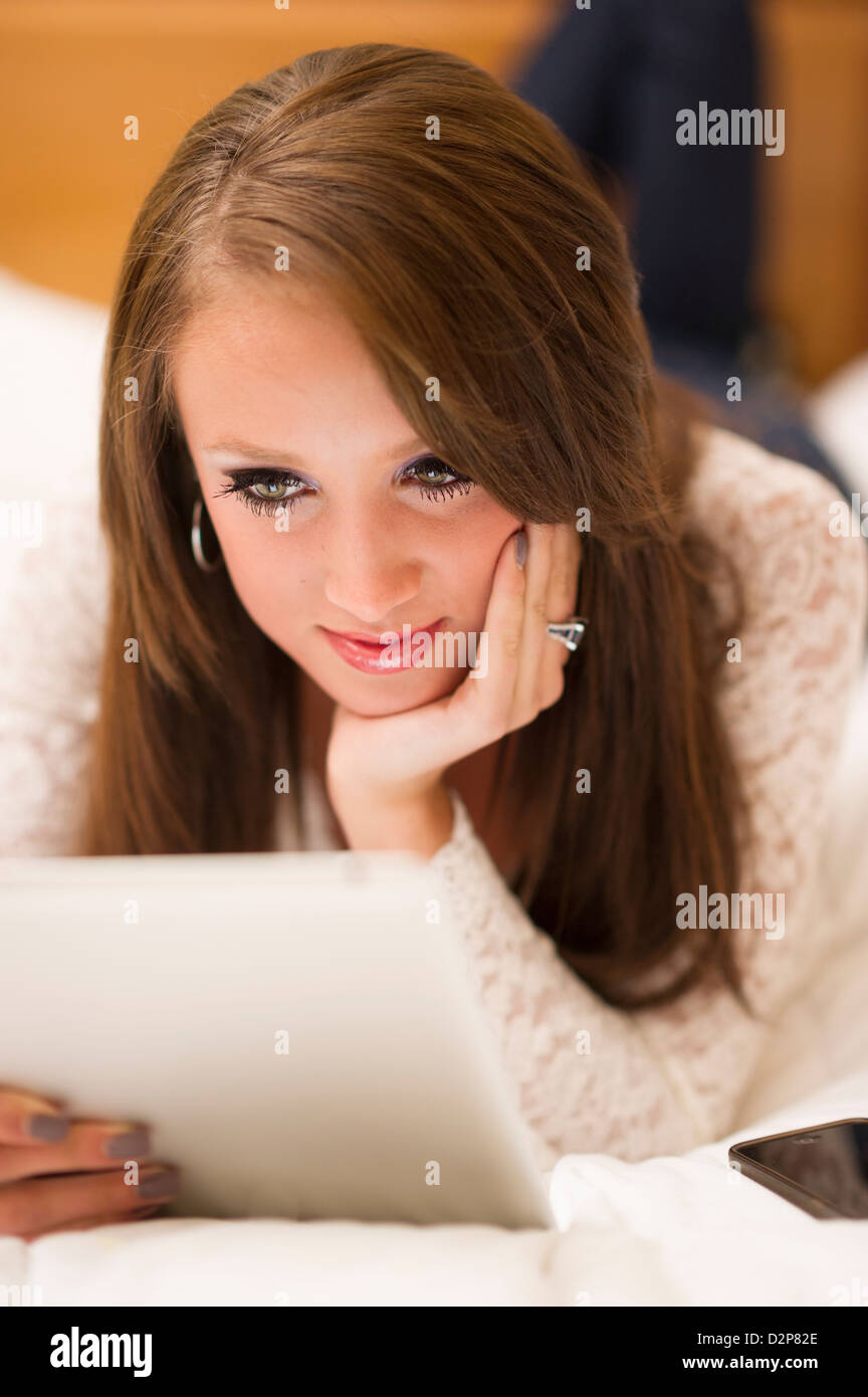 Schönes junges Mädchen lag auf einem Bett auf einem Tablet-PC. Stockfoto
