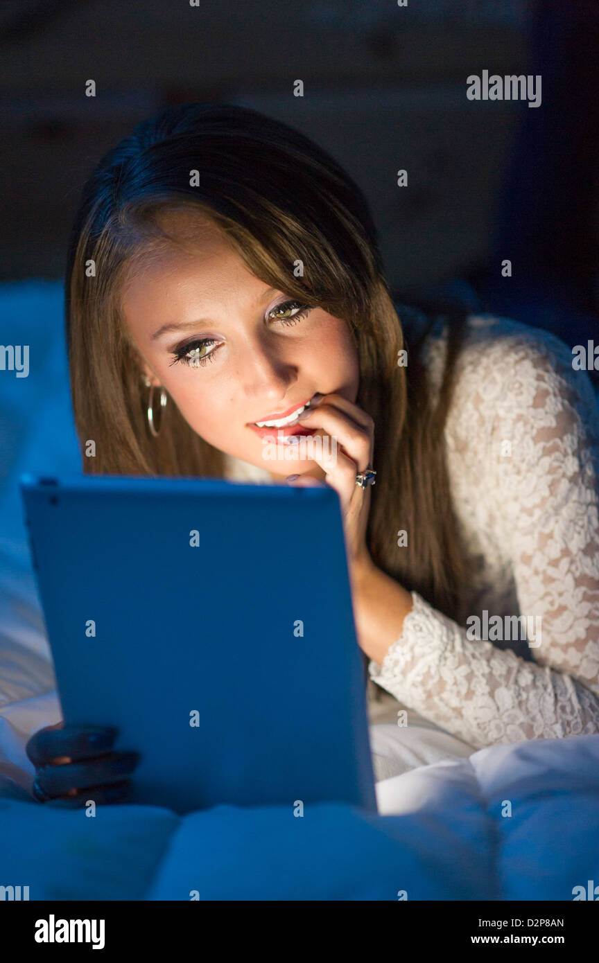 Schöne Mädchen im Teenageralter im Dunkeln liegen auf einem Bett auf einem Tablet-PC. Stockfoto